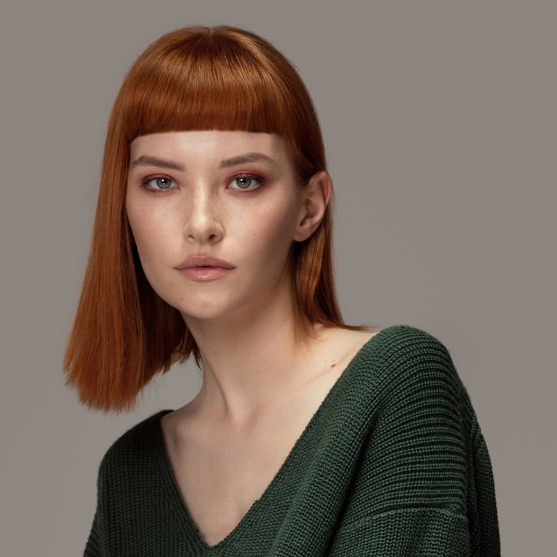 Retrato de estúdio de mulher branca com cabelo ruivo curto e franja reta.