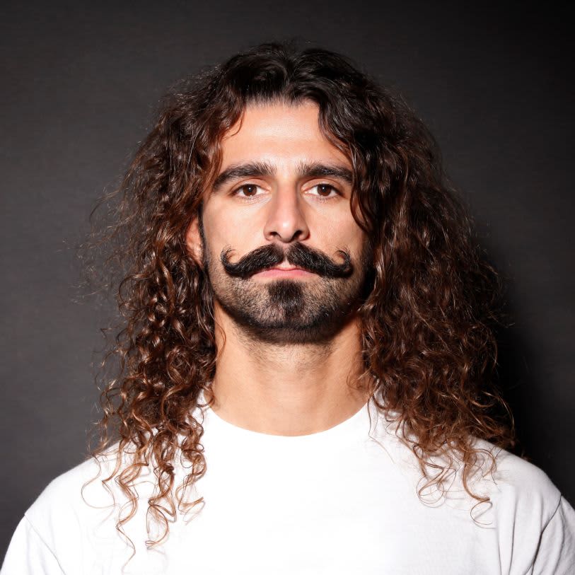 Homem com cabelos longos cacheados e bigode grande com as pontas viradas para cima.