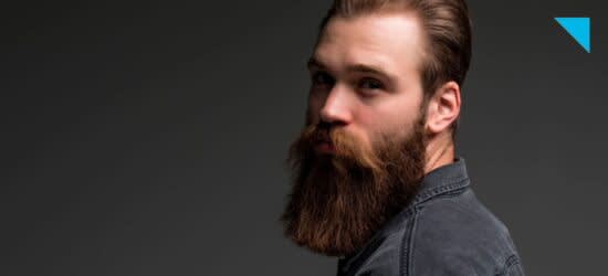 Homem em fundo cinza com barba longa e cabelo castanho. Veste uma camisa jeans também cinza.