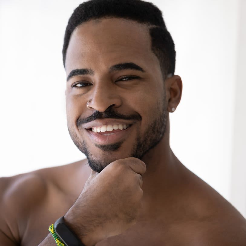 Homem sorridente com bigode e barba bem cuidada, tocando o queixo.