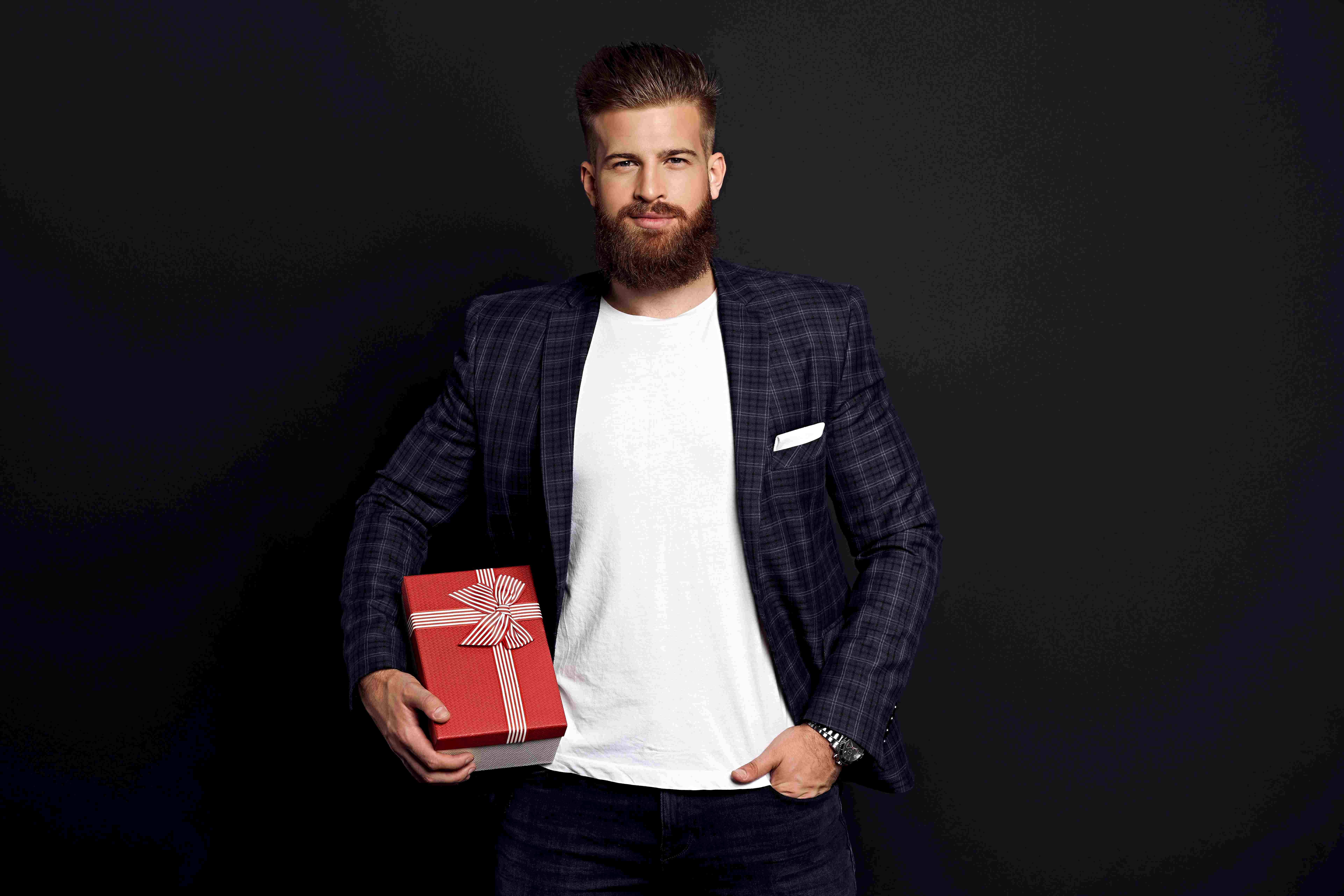 Homem branco com barba cheia segurando uma caixa de presente vermelha