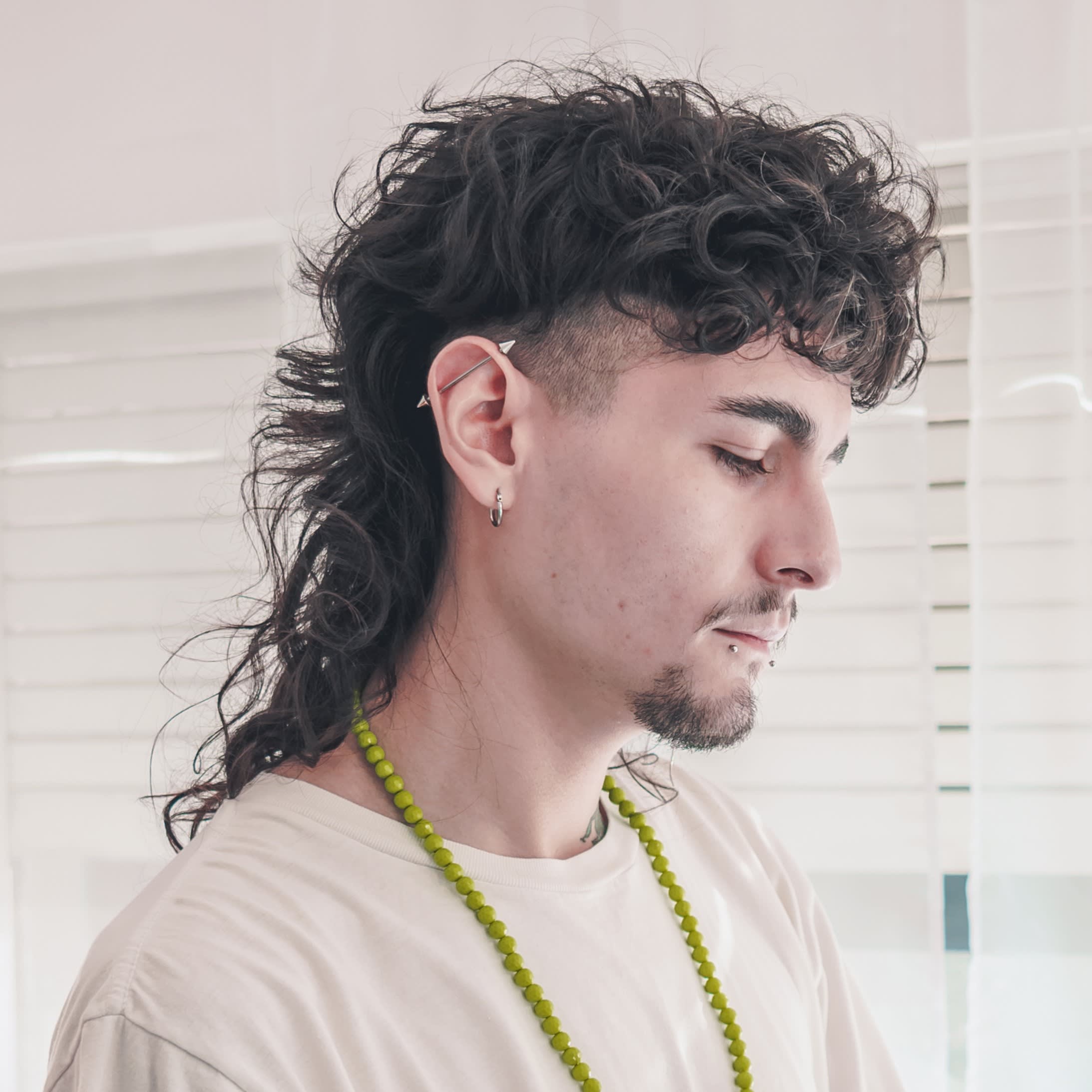 Jovem com cabelo cacheado e longo usando corte de cabelo mullet masculino