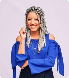 Na imagem Larissa, aluna formada, é uma mulher negra sorridente, com cabelos trançados de tamanho médio em tom loiro. Está usando uma blusa azul