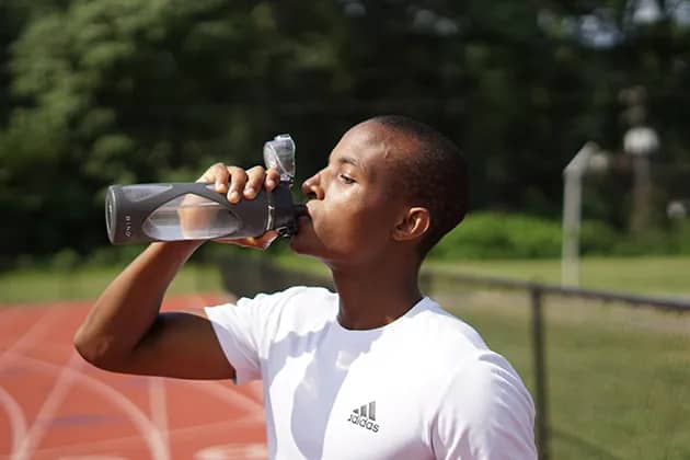 Foto de jovem negro tomando água em pista de atletismo.