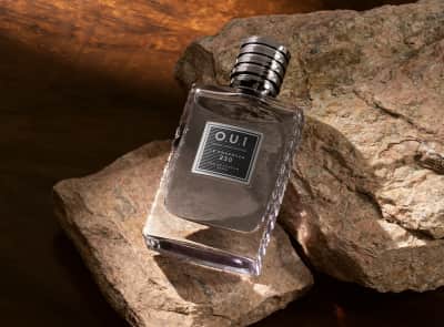 Um frasco do Le Charmeur 250 Eau de Parfum. O produto está posicionado sobre uma rochosa.