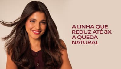A imagem mostra uma mulher sorrindo com cabelos longos e escuros. A linha que reduz até 3x a queda natural.
