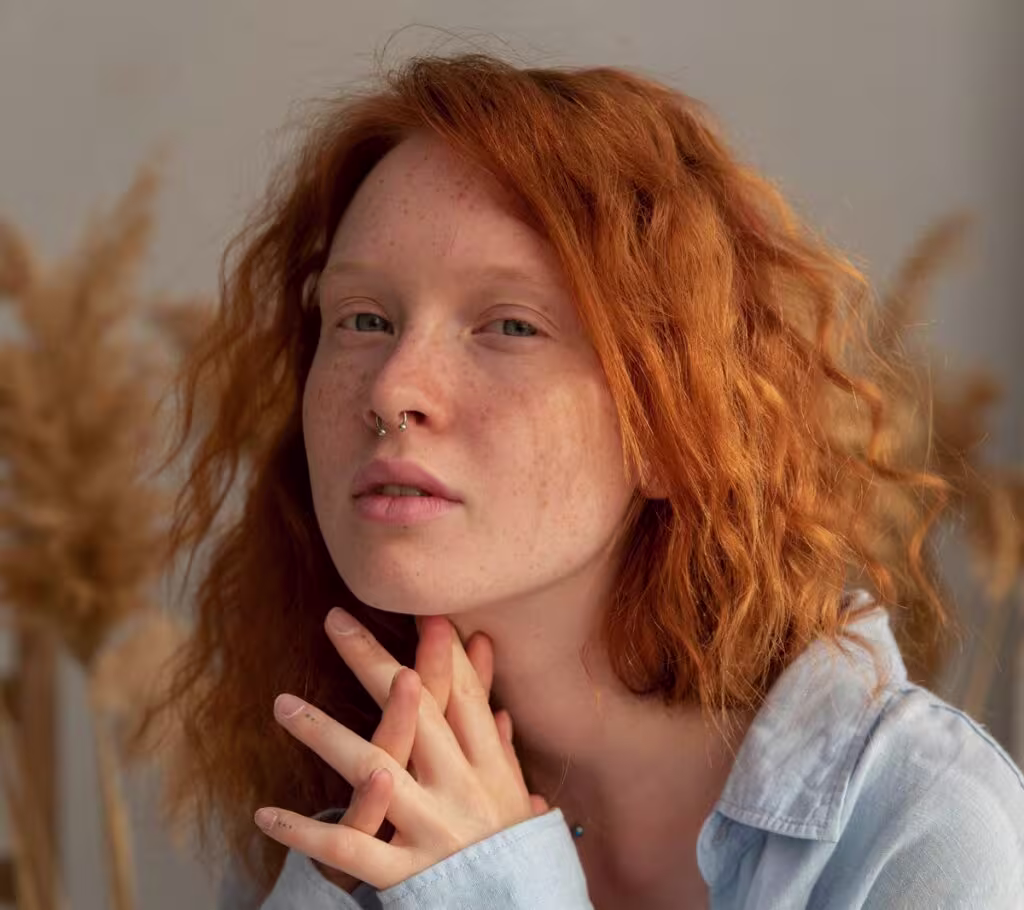 Mulher ruiva com cabelo ondulado e piercing no septo.