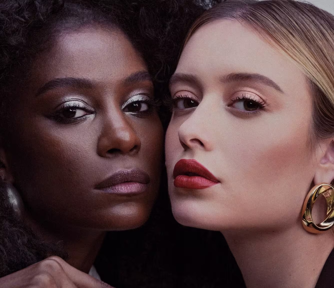Na Semana de Moda Eudora, duas modelos estão olhando para a câmera com as maquiagens do lançamento no rosto. Uma modelo tem a pele preta e a outra modelo tem a pele branca, ambas usam mix de metais que são o conceito de Eudora Glam Metals.