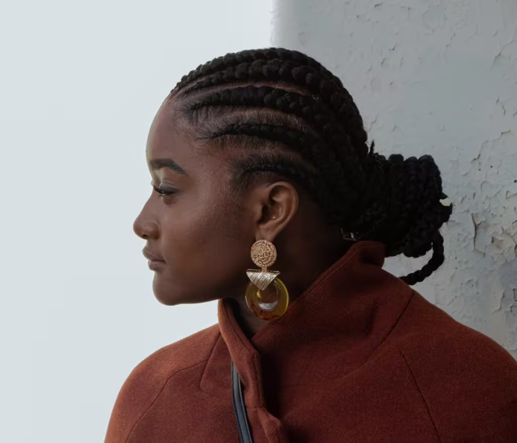 Mulher de perfil com tranças presas num coque e brincos grandes.