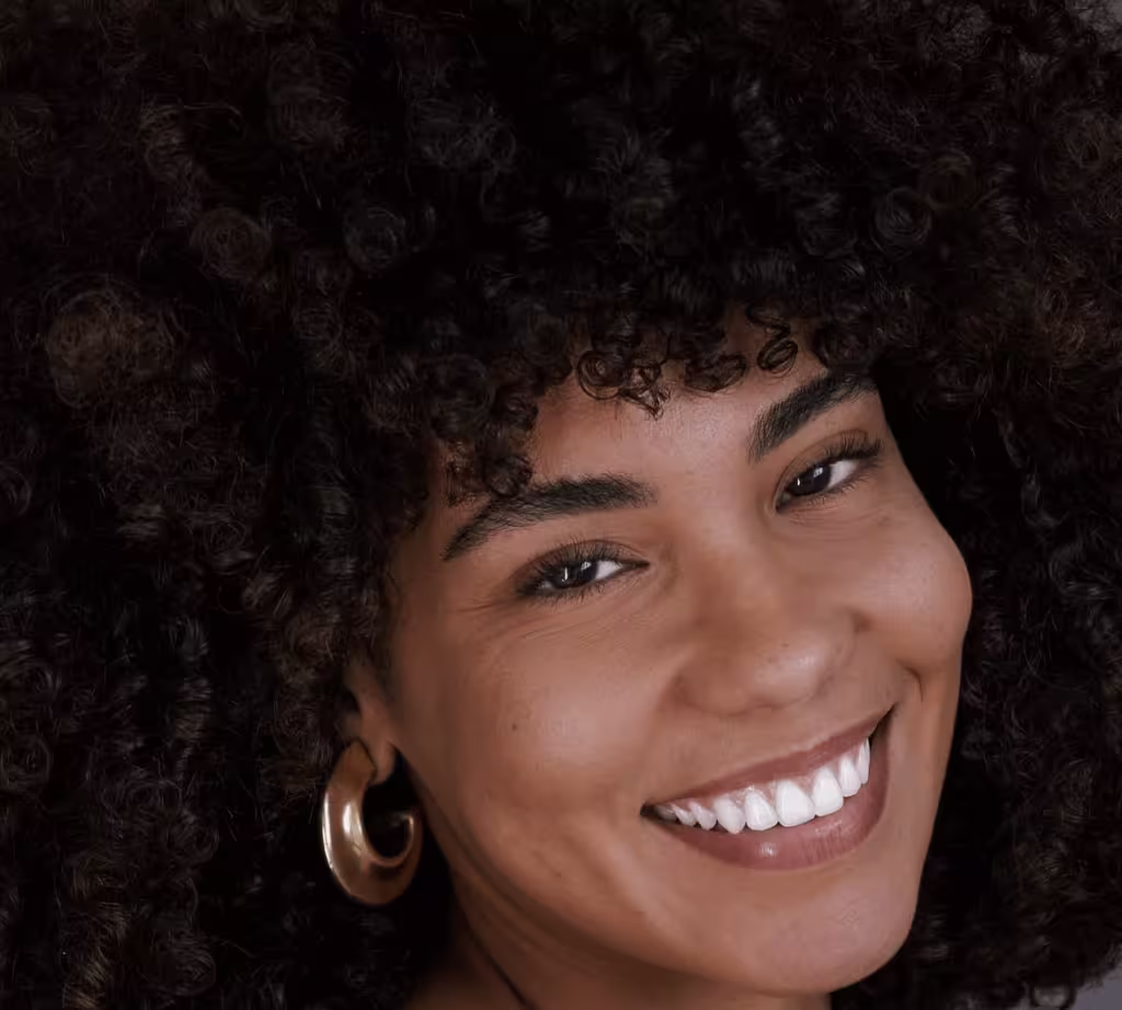 Duda Lisboa com cabelo solto bem cacheado olhando com sorriso simpático para a foto.
