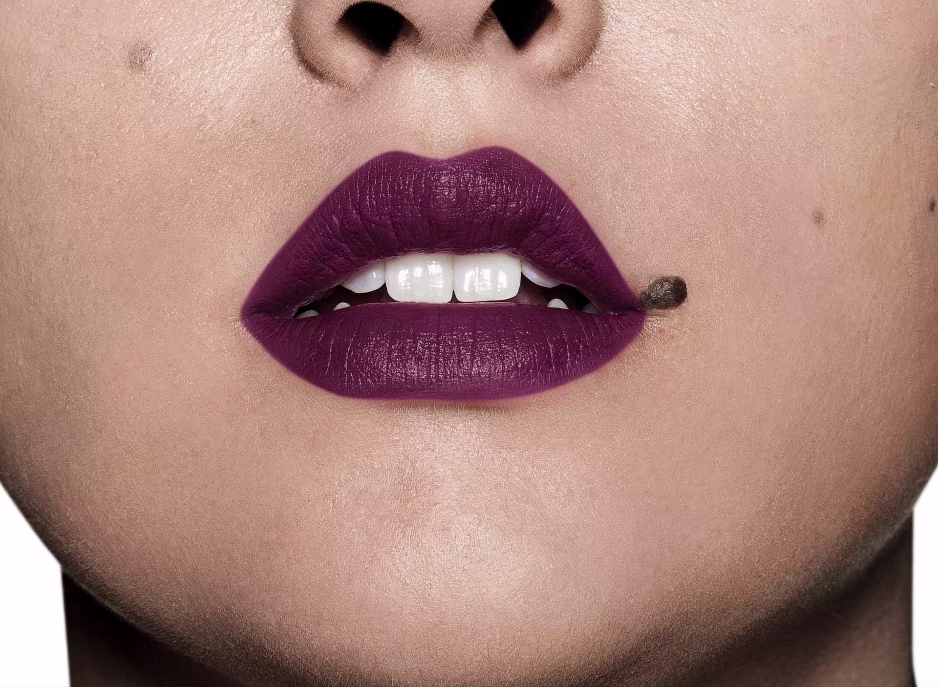 Batom cremoso Intense Malva. A imagem foca na boca da modelo, que é branca com uma pinta na lateral dos lábios.