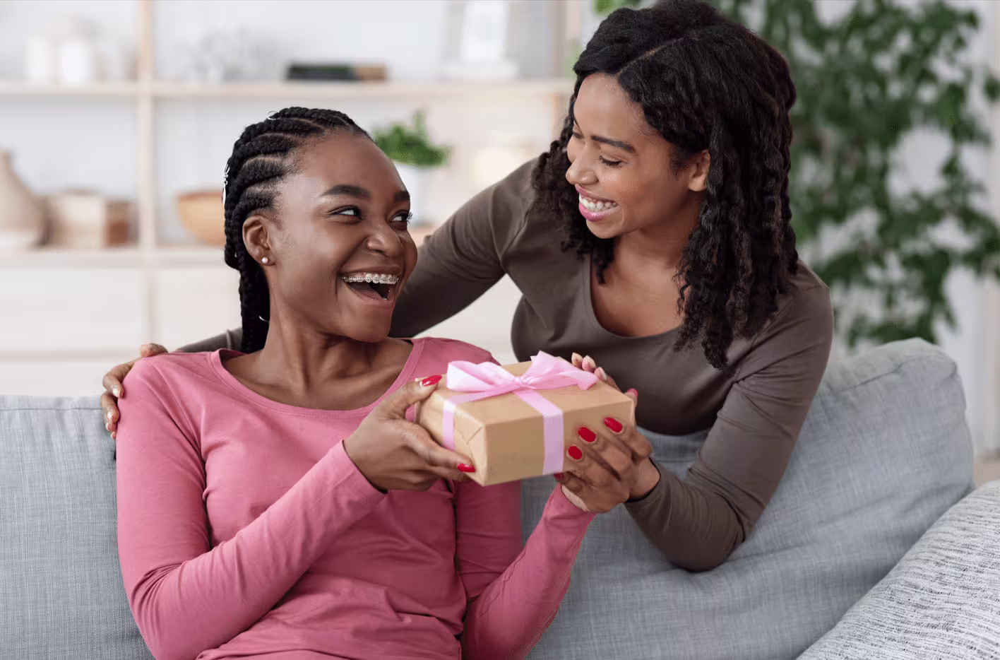 Imagem de duas mulheres felizes e sorrindo, uma delas está entregando um presente para a outra.