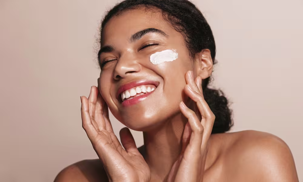 Imagem de mulher sorridente aplicando hidratante facial