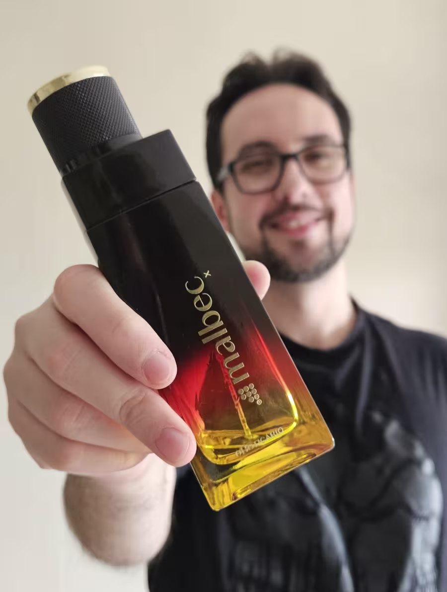 Luiz Ribas, homem branco, de cabelos castanhos, barba e óculos, segurando o frasco de Malbec X