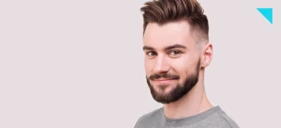 Foto de homem de camisa cinza em fundo neutro, cabelo raspado na lateral, meio sorriso e barba degradê.