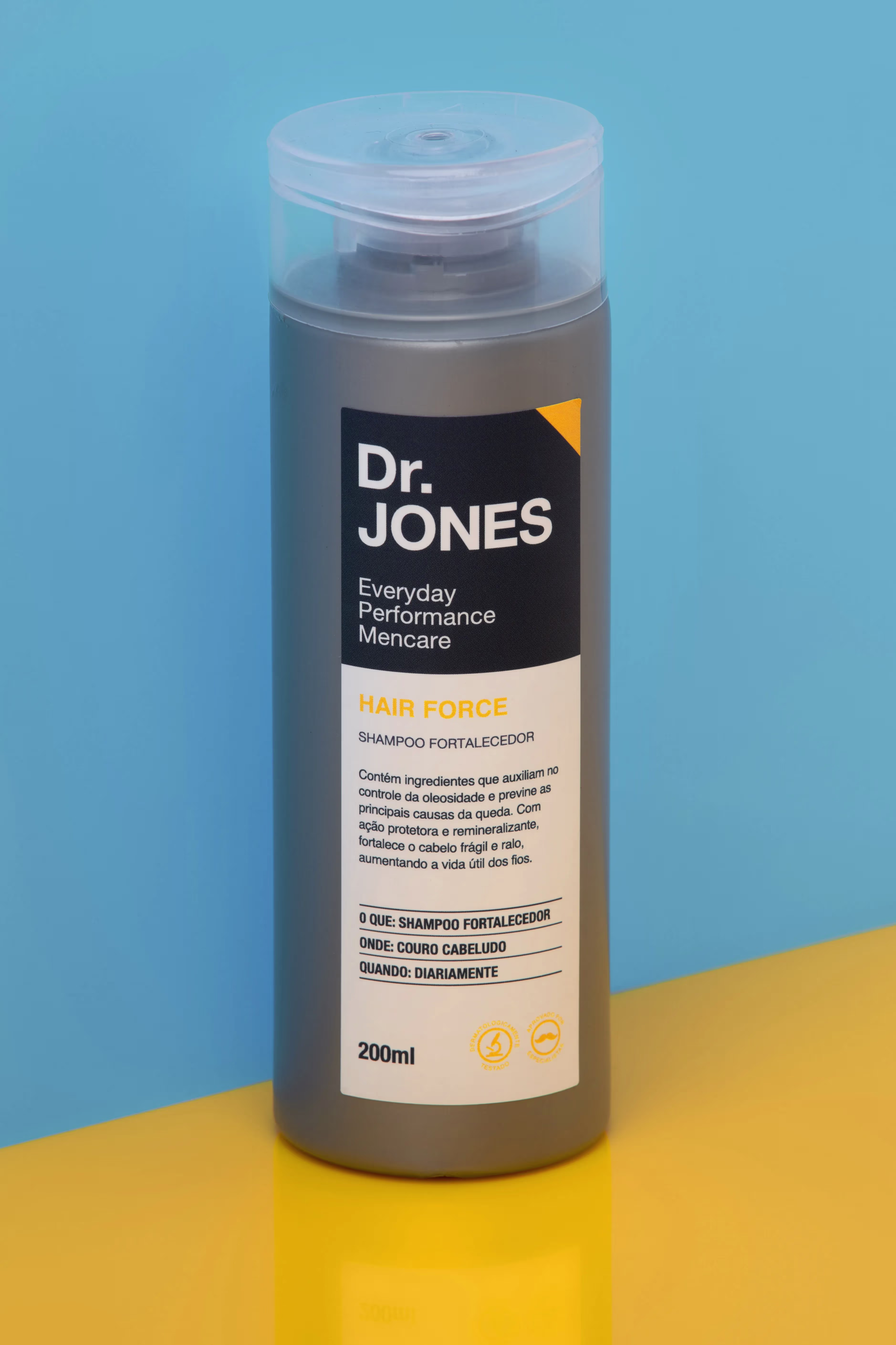 Em fundo dourado com paredes azul-claras, foto destaca a embalagem do shampoo fortalecedor HAIR FORCE, da Dr. JONES, que contém Capalgin em sua formulação.