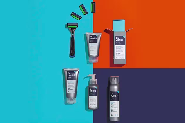 Foto de produtos da linha de barba da Dr. JONES: The Razor, The Shaving Solution, Precision Foam e Recharge After-Shave e The Razor6, em fundo geométrico laranja, azul-escuro e azul-claro.