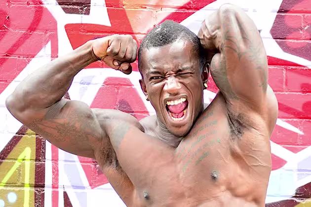 Em artigo sobre como calcular proteínas para ter massa muscular, homem negro de torso nu põe braços às costas, músculos evidentes, em frente a parede com graffiti