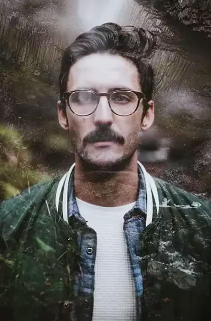 Composição de foto de homem de pele clara, óculos escuros e bigode grosso, olhos claros, olhando para a câmera, com elementos da natureza e uma cachoeira passando por entre sua imagem.