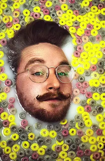 Foto de homem de pele clara, cabelo escuro voltado para cima e bigode curvado também para cima e barba em banheira com leite e produtos para limpeza da pele. Ele está imerso e apenas o rosto está para fora.