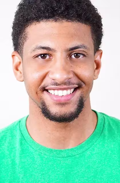 Foto de homem pardo, camiseta ciano, sorrindo, cabelos escuros e cavanhaque.