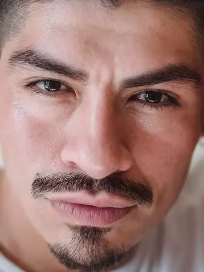 Foto em que se destaca o rosto de homem de pele clara com "barba âncora", isto é, cavanhaque e bigode desconectado do restante, olhando direto para a câmera e usando camiseta branca.