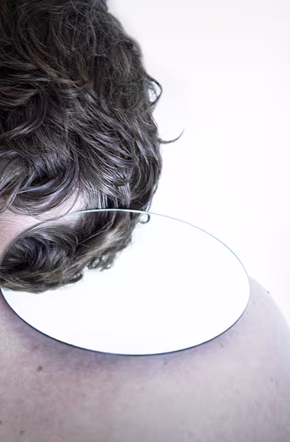 Foto que mostra um cabelo ondulado castanho em destaque, com espelho, que ressalta necessidade de acompanhamento dermatológico para queda de cabelo e calvície.