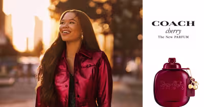 A imagem mostra o novo Coach Cherry Parfum, perfume de frasco vermelho com a tradicional carruagem Coach estampada na frente.