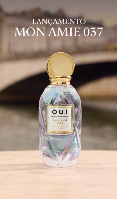 Lançamento Mon Amie 037, frasco de Eau de Parfum com tampa dourada esférica, vidro transparente com efeito iridescente em tons pastel de azul, rosa e roxo, rótulo branco com logotipo OUI e indicação 037, posicionado sobre superfície clara com ponte arquitetônica desfocada ao fundo.