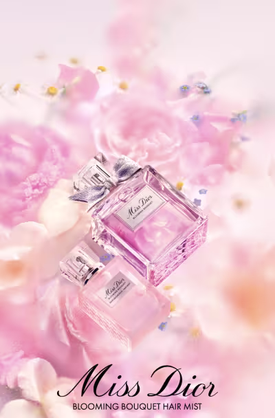 A imagem apresenta uma composição de flores rosas e brancas, com um frasco de perfume da marca Miss Dior no centro. O frasco possui um laço prateado e a embalagem exibe o nome da fragrância em destaque. Abaixo, há informações sobre uma oferta promocional que inclui uma amostra e uma miniatura do produto.