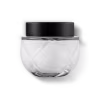 Frasco de vidro transparente arredondado com tampa preta. A embalagem tem um design minimalista e clean, com linhas suaves e uma forma esférica. As cores predominantes são o preto da tampa e o transparente do vidro e a cor branca do creme.