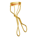 Produto de maquiagem da marca Shiseido. Objeto dourado em forma de curvador de cílios. Possui uma faixa vermelha com o nome "Shiseido" gravado em letras maiúsculas.