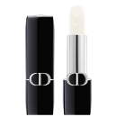 A imagem mostra uma embalagem de balm labial, tipo bala, branco, com a tampa ao lado. A embalagem é preta e prata com o logo da marca em prata.