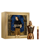 O produto apresentado é um perfume da marca Jean Paul Gaultier. Ao lado do frasco, há uma caixa dourada com uma imagem de uma pessoa vestida com uma camiseta preta com o nome da marca e calças xadrez. E uma versão tamanho viagem do perfume.