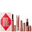 Caixa rosa com produtos de maquiagem da marca M·A·C, incluindo batom, gloss labial e outros itens em tons de rosa e marrom. A embalagem apresenta um design geométrico em vermelho e branco.