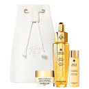 Conjunto de itens de perfumaria da marca Guerlain, incluindo um frasco de vidro dourado com rótulo "Abeille Royale", um pote de creme branco com rótulo "Abeille Royale Honey Treatment", e uma bolsa branca com cordão.