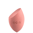 Esponja de maquiagem de cor rosa, com formato assimétrico e textura macia, com o logotipo "O.C.N." impresso na superfície.