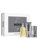Conjunto de produtos de beleza da marca Boss, contendo um frasco de perfume, um gel de banho e um desodorante em embalagens de cores cinza e amarela.