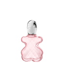 Frasco de item de perfumaria com formato curvilíneo em vidro rosa translúcido, com tampa prateada e rótulo com a marca "TOUS" em destaque.