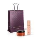 Conjunto de produtos Eudora da linha Magnific, incluindo um frasco de spray corporal e um pote de creme, embalados em uma sacola de compras roxa com padrão geométrico.