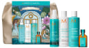 Caixa e embalagens de produtos Moroccanoil em tons de azul e verde, incluindo frascos de shampoo, condicionador e óleo para cabelos. Rótulos e ilustrações com estilo artístico e elementos decorativos.
