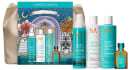 Conjunto de produtos Moroccanoil em embalagens com design ilustrativo, incluindo frascos de shampoo, condicionador e óleo hidratante em tons de azul e laranja, com rótulos e textos descritivos.