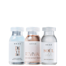 A imagem mostra três frascos de vidro transparente com tampas brancas, contendo líquidos de diferentes cores - branco, rosa e incolor. Os frascos têm rótulos com o nome da marca "BRAÉ" e os nomes das linhas: "Divine", "Revival" e "Soul Color".