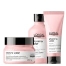 A imagem apresenta a linha Vitamino Color, da L’Oréal Professionnel, para cabelos coloridos: shampoo (frasco), tratamento (pote) e condicionador leave-in (tubo), todos em embalagens rosa claro com tampa preta.