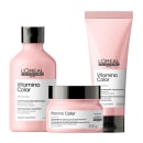 A imagem apresenta a linha Vitamino Color, da L’Oréal Professionnel, para cabelos coloridos: shampoo (frasco), tratamento (pote) e condicionador leave-in (tubo), todos em embalagens rosa claro com tampa preta.