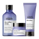 A imagem mostra três produtos da linha Blondifier da L'Oréal Professionnel. Um shampoo em um frasco azul transparente de 300ml, um condicionador em um tubo roxo opaco de 200ml e uma máscara em pote redondo azul. Todos possuem tampa preta.