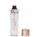 A imagem mostra o frasco do fixador de maquiagem aberto com a tampa ao lado, é uma embalagem transparente e cilíndrica, com o nome da marca e o texto "Océane" gravados nele. A tampa é de cor rosé gold e as letras do rótulo são douradas.