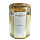 Vela natural de cera amarela em frasco de vidro cilíndrico transparente. Rótulo branco com o nome do produto "Amarula, Super Premium" e a marca "Perfuma & Decora". Cores predominantes são amarelo claro da cera, branco do rótulo e transparente do vidro.