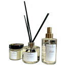 Na imagem três produtos Perfuma & Decora. Um frasco de vidro transparente com tampa dourada com home spray. Ao lado, há um difusor de aromas em um frasco de vidro transparente e varetas pretas e um pote de vidro transparente com uma vela perfumada.