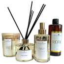 Linha de produtos de aromatização ambiental da marca Perfuma & Decora. Inclui difusores de aromas com varetas, um frasco de vidro âmbar para refil, um frasco de vidro transparente com tampa dourada para difusor, uma vela perfumada em vidro transparente.